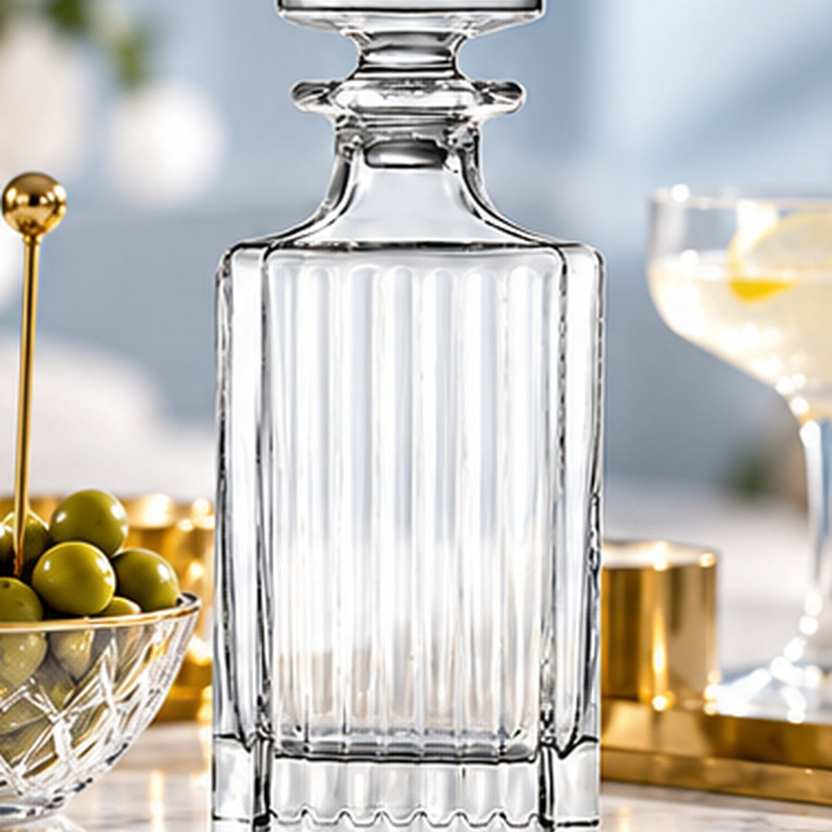 Carafe RCR Timeless sur un plan de marbre, bol d'olives et coupe de cocktail en arrière-plan