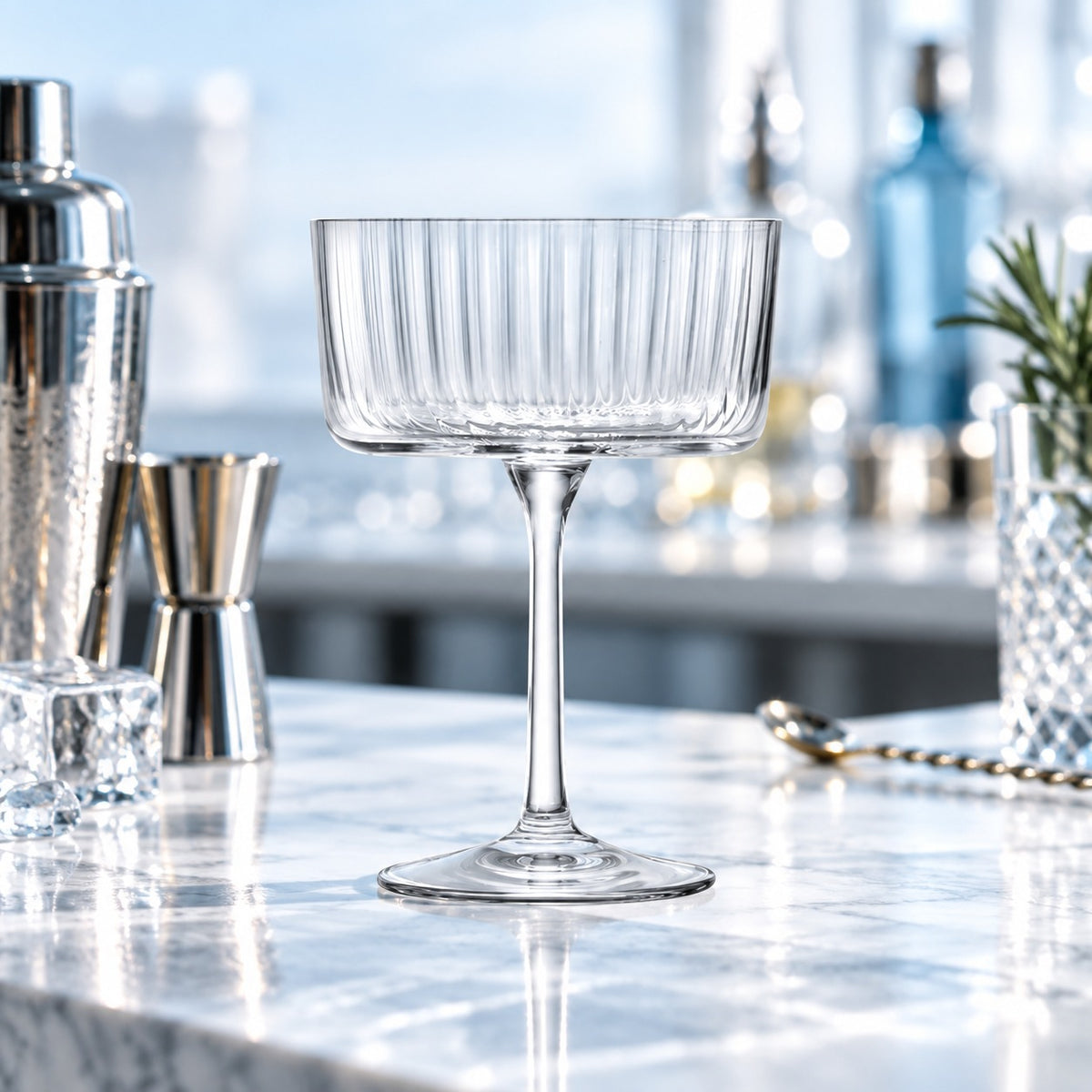 Coupette Gio Line vide sur un bar en marbre avec shaker, jigger et cuillère de bar
