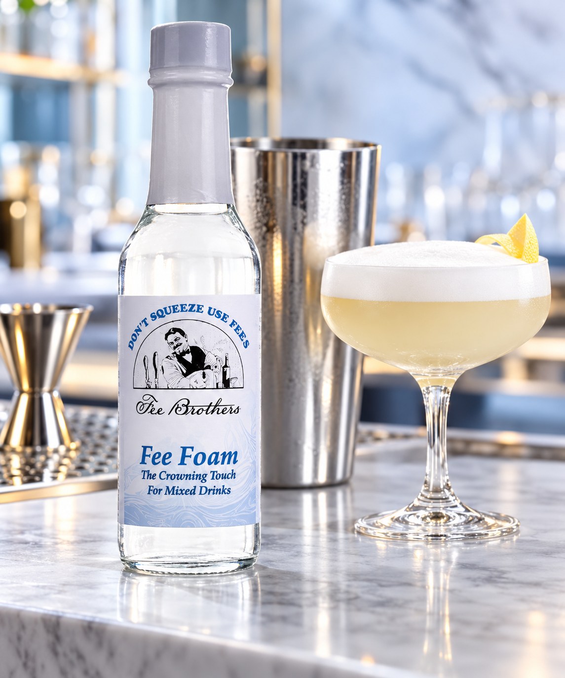 Flacon de Fee Foam à côté d'un shaker inox et d'un cocktail mousseux sur un plan de marbre