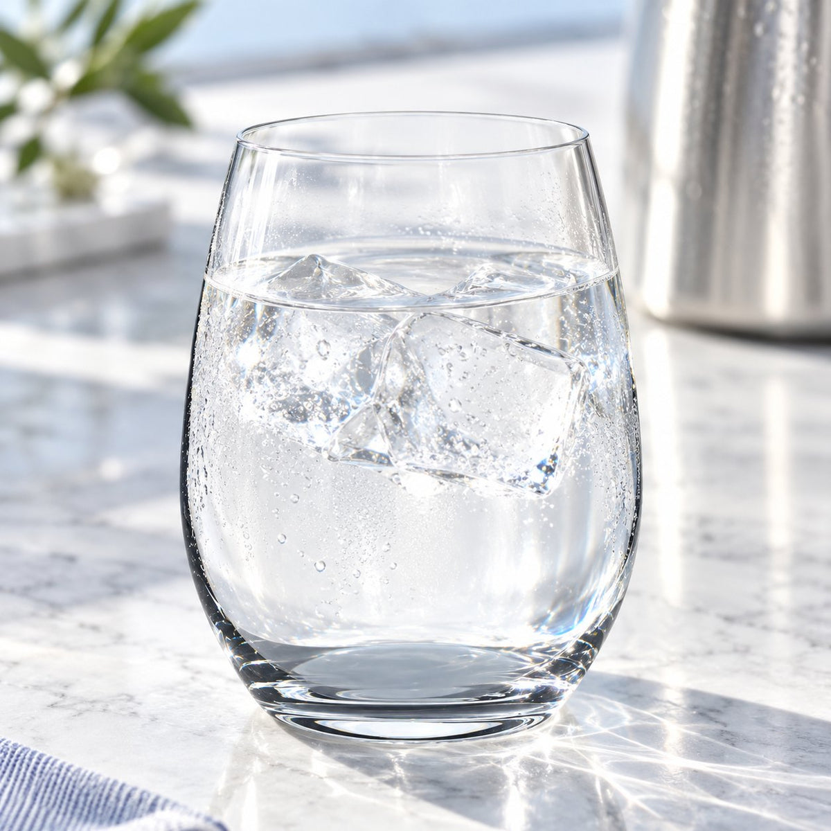 Verre à eau Nude Pure rempli d'eau et de glaçons sur un comptoir en marbre