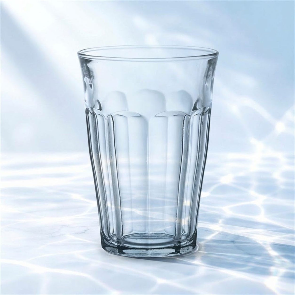 Verre à bière Lehmann Craft de 44 cl debout sur un marbre blanc avec reflets d'eau, fond bleu clair