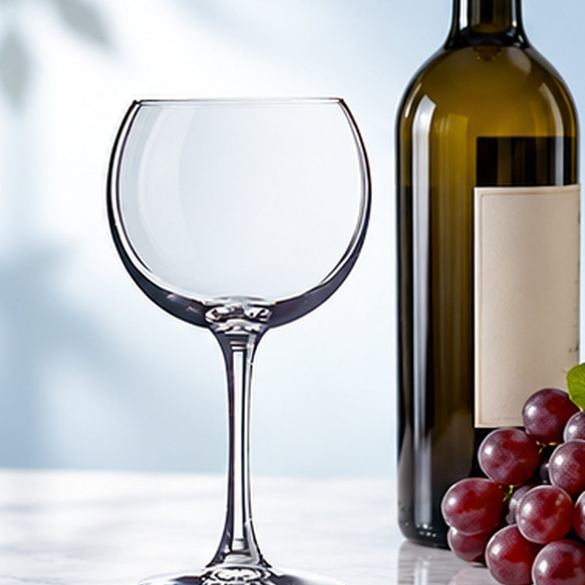 Verre à vin ballon Chef & Sommelier Cabernet vide à côté d'une bouteille de vin et de raisins sur un plan de marbre