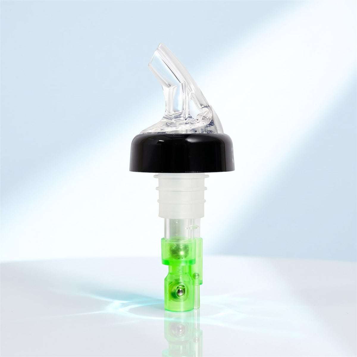 Bec verseur doseur à bille transparent avec bague noire et base verte, debout sur une surface blanche brillante