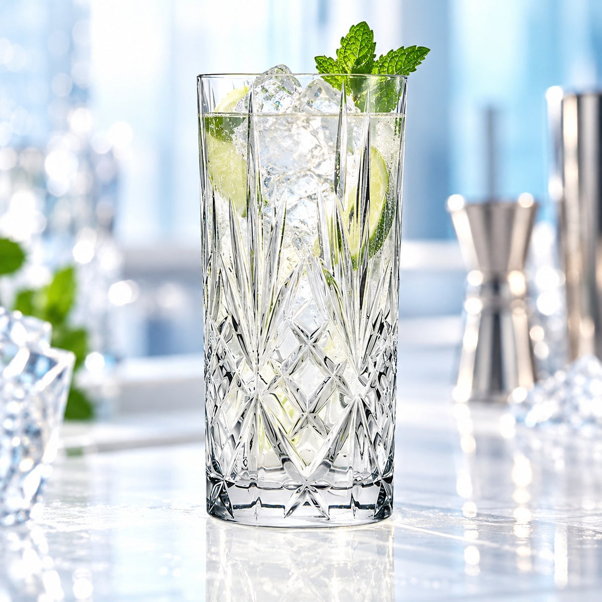 Verre long drink RCR Melodia rempli de glaçons, de citron vert et de menthe sur un plan de marbre, jigger en arrière-plan