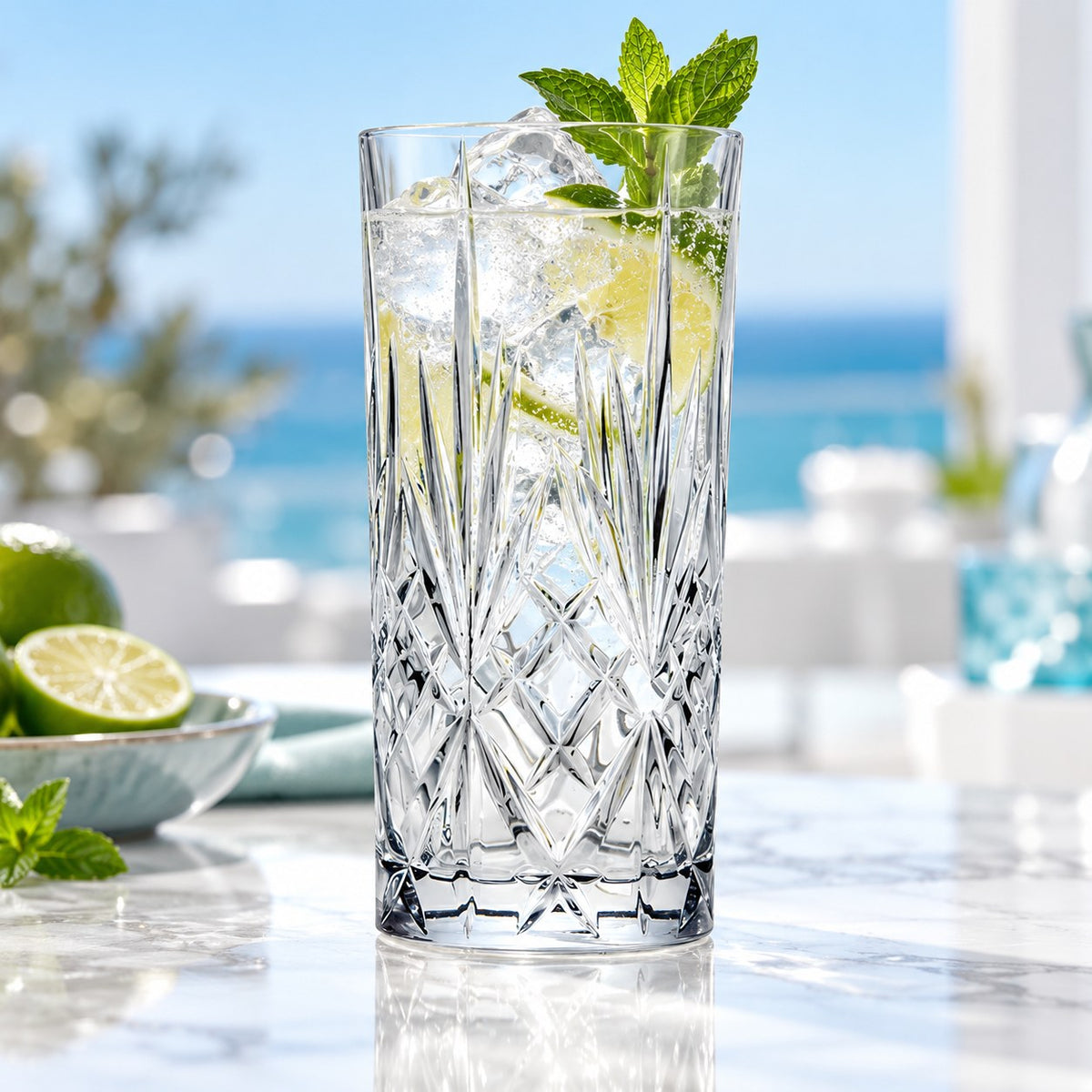 Verre long drink RCR Melodia rempli de glaçons, de menthe et de citron, vue sur la mer