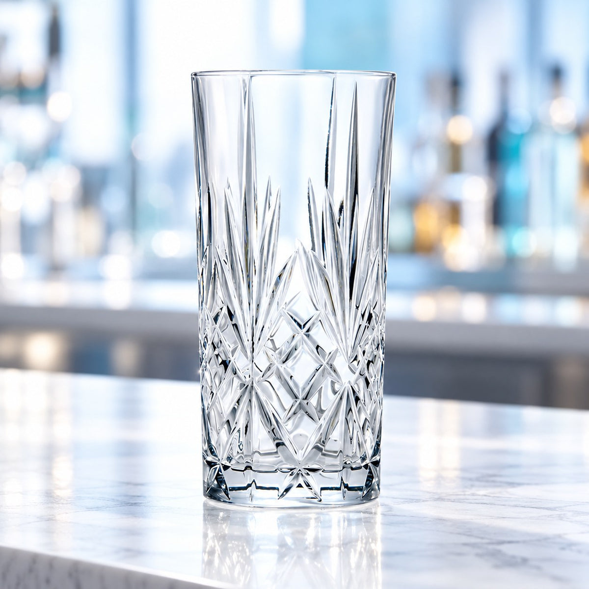 Verre long drink RCR Melodia vide sur un plan de marbre devant des bouteilles de bar