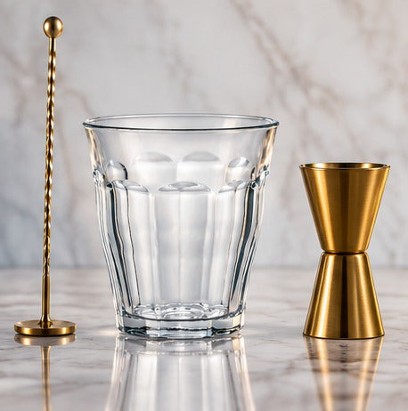 Long drink Duralex Picardie 31 cl, à côté d'un bar spoon et d'un jigger doré