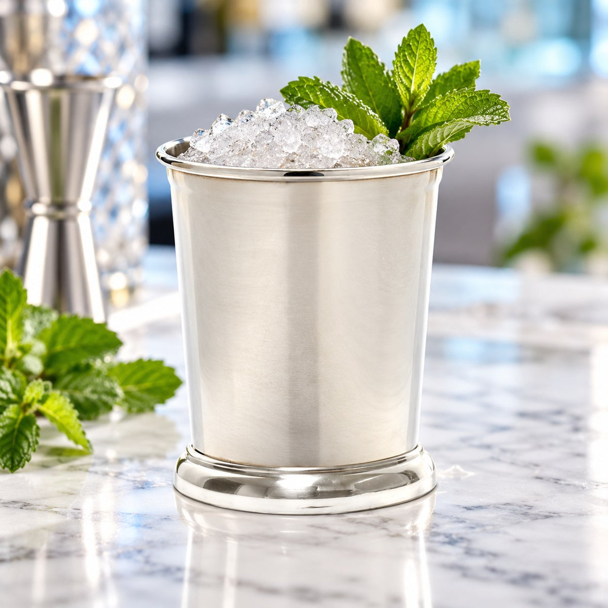 Julep Cup argent rempli de glace pilée et de menthe sur un plan de marbre, jigger en arrière-plan