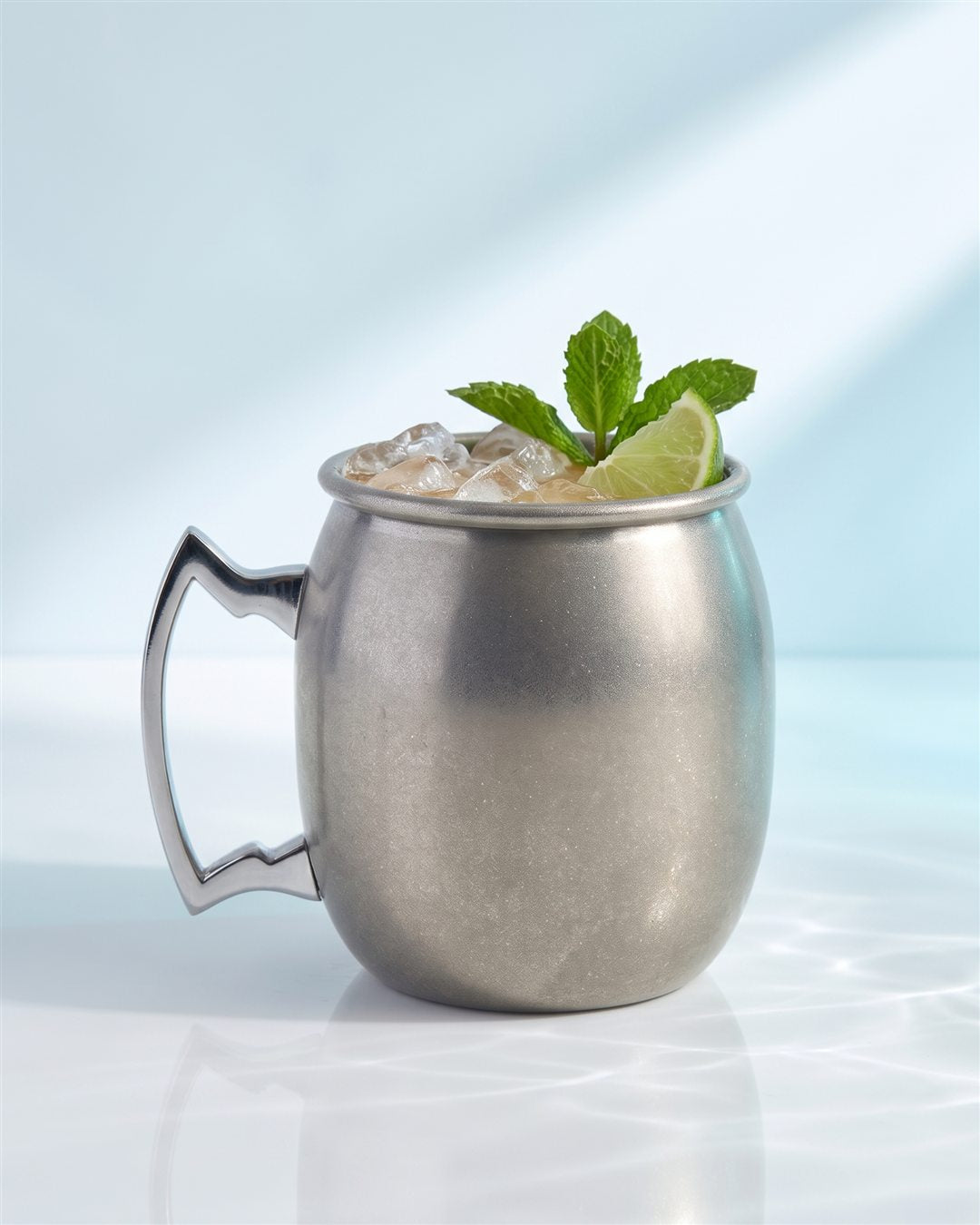 Mug Moscow mule rempli de glace pilée avec une tranche de citron vert et une tige de menthe sur un comptoir blanc