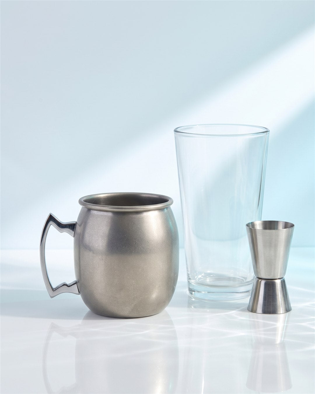 Mug Moscow mule argent à côté d'un verre de bar et d'un jigger inox pour situer sa taille