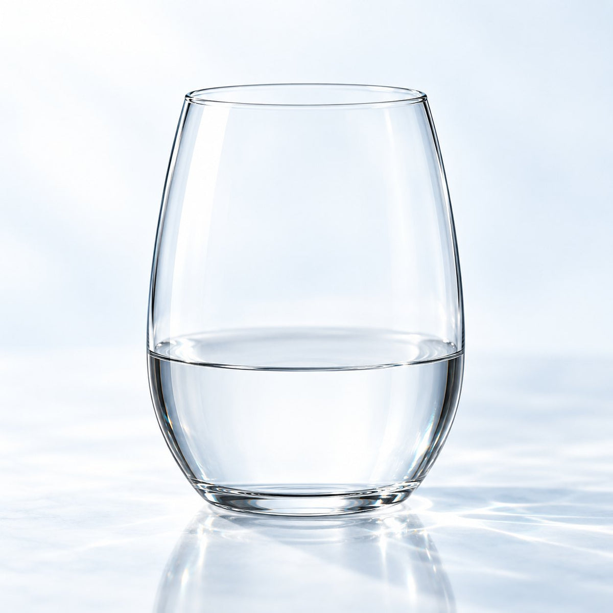 Verre à eau Nude Pure 25 cl sans pied, rempli d'eau, vu de face sur un plan de marbre lumineux