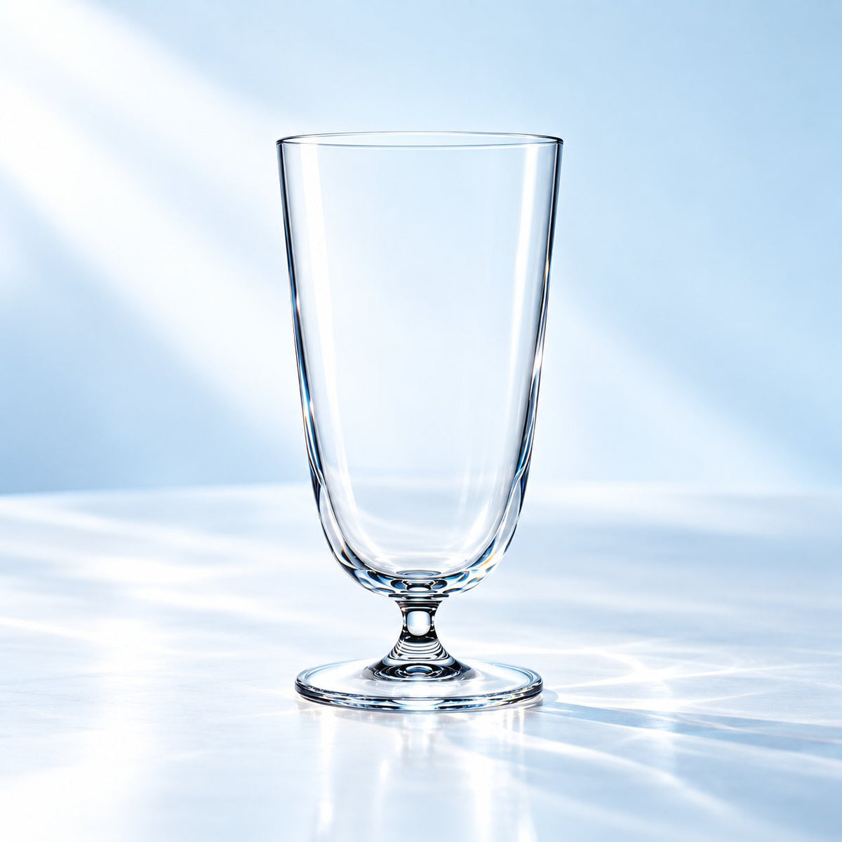 Verre à cocktail long Nude Bar Giani 37 cl sur pied court, vu de face sur un plan de marbre lumineux