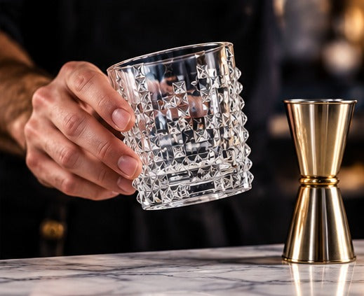 Short drink Nachtmann Punk 35 cl, en main, à côté d'un jigger doré