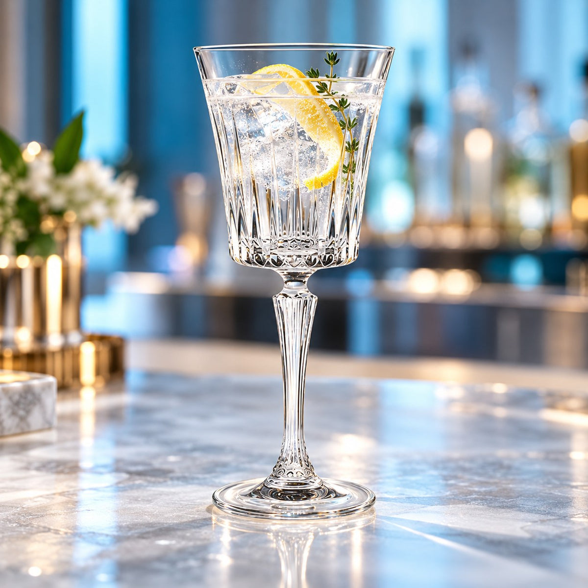 Verre à cocktail RCR Timeless rempli d'un cocktail avec glaçons, citron et thym sur un comptoir en marbre