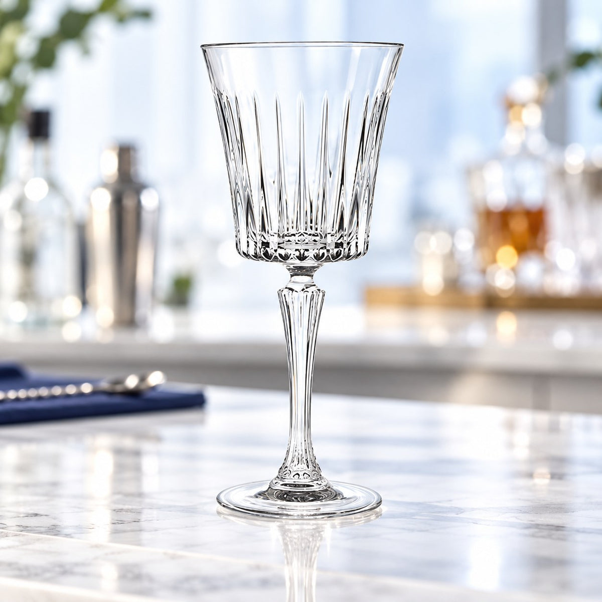 Verre à cocktail RCR Timeless vide sur un comptoir en marbre devant des bouteilles de bar