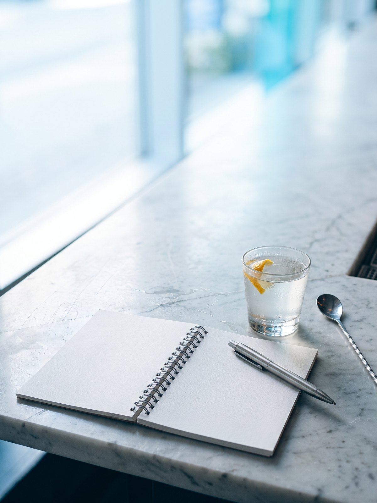 Blog BWA, actualités et conseils du bar : carnet ouvert, stylo, verre de cocktail et cuillère de bar sur un comptoir en marbre