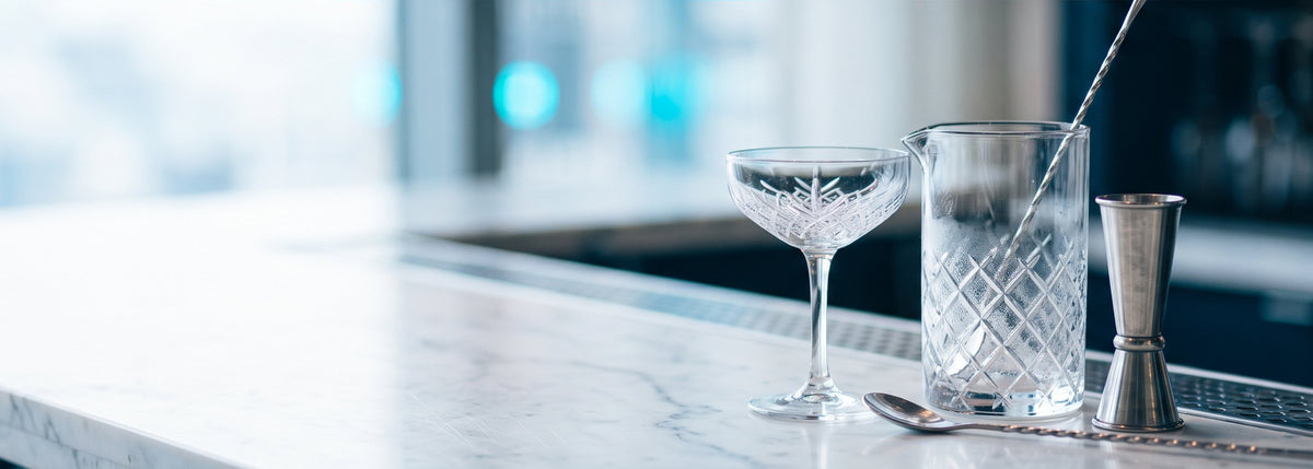 BWA, nouvelle identité : verrerie et matériel de bar professionnel, verre à mélange en cristal, jigger et cuillère de bar sur un comptoir en marbre blanc